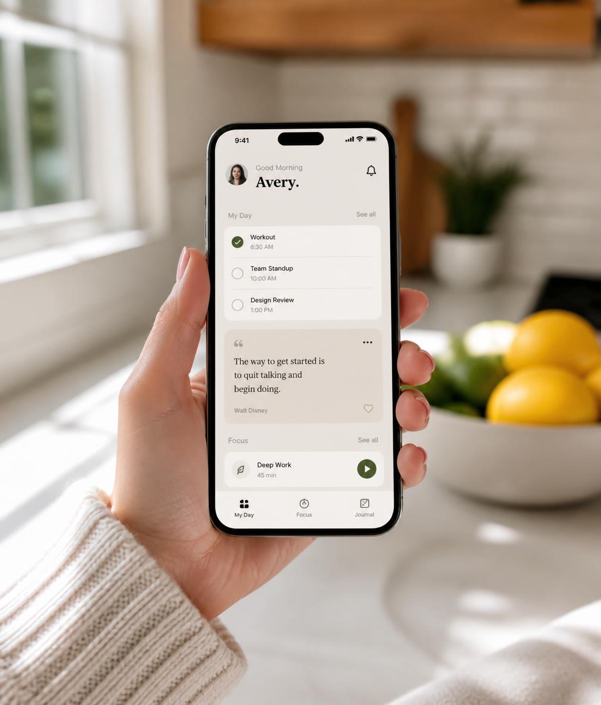 A person holding a phone showing a minimal daily planner app in a sunlit kitchen